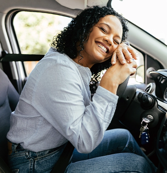 Woman enjoying new car hugging steering wheel sitting inside