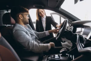 Man sitting in a new luxury car he is considering purchasing with a car loan, helped by car dealership sales person