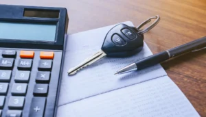 Car loan tax deductions depicted by a calculator, paperwork, and a car key next to a pen.